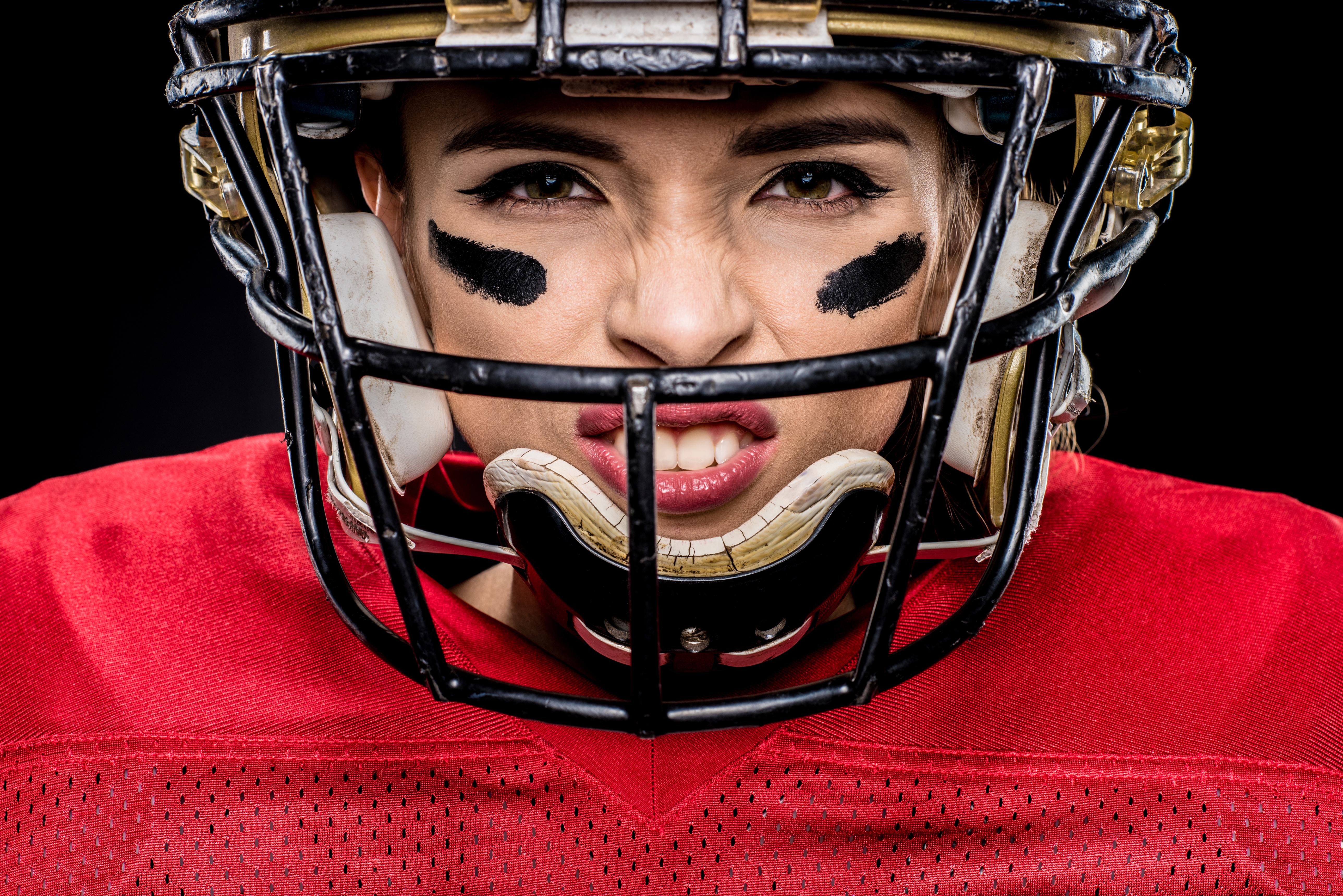 Close-up portrait of female american football player in sportswear and helmet on black